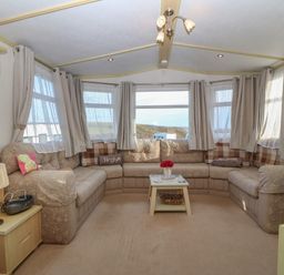 A living room with a corner sofa a coffee table a lamp and multiple windows at Tir Glyn Caravan in Uwch Mynydd near Aberdaron