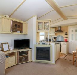 A living room with a television sofa dining table and kitchen area at Tir Glyn Caravan in Uwch Mynydd near Aberdaron