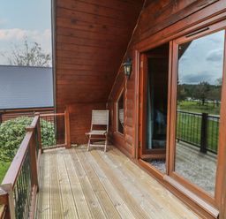 A wooden balcony with a chair and glass door overlooking grass and trees at Cedar in Dolton
