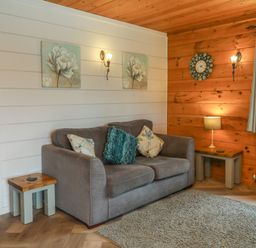 A living room with a gray sofa and cushions two side tables a lamp a wall clock and flower paintings at Pine in Dolton
