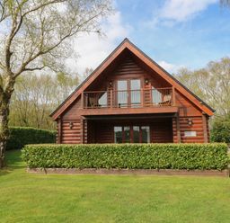 A wooden cabin with a balcony and green hedges in front at Willow in Dolton