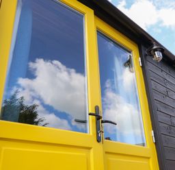 Yellow double doors with glass panels on a black wooden building exterior at Tower Hut in Ryde