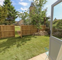 A garden with grass wooden fence a small tree and a stone pile visible from an open door at Tower Hut in Ryde