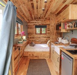 A small wooden interior with a bed at the end and a kitchenette on the right at Tower Hut in Ryde
