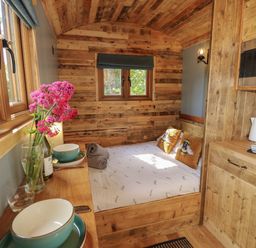 A small wooden room with a bed, kitchen counter, microwave, kettle, bowls, and flowers on a table at Tower Hut in Ryde