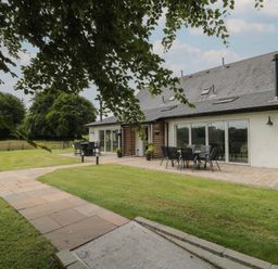A garden patio area with tables and chairs outside a house with large windows at Primrose Cottage in Brendon Hill near Roadwater