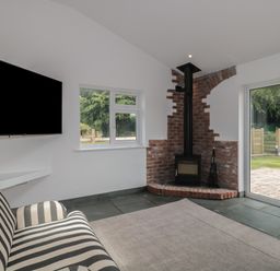 A living room with a striped sofa a wall-mounted television a brick fireplace and glass doors at Primrose Cottage in Brendon Hill near Roadwater