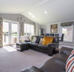 A living room with leather sofas pillows and patio doors overlooking water at Capenwray in Carnforth