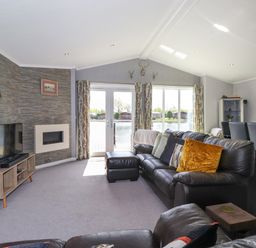 A living room with leather sofas a TV and fireplace next to glass doors leading outside at Capenwray in Carnforth