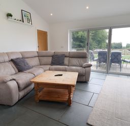 A living room with a gray sectional sofa wooden coffee table and sliding glass doors opening to an outdoor patio at Campion Cottage in Brendon Hill near Roadwater