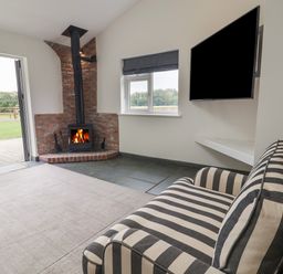A room with a striped sofa a wood burning stove window and a wall mounted television at Campion Cottage in Brendon Hill near Roadwater