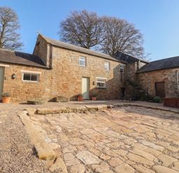 An outdoor area with buildings and stone path at Cragg Lodge in West Woodburn