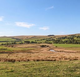 A landscape with hills, fields, and a stream at Cragg Lodge in West Woodburn