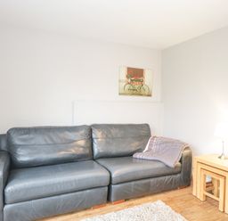 A living room with a leather sofa a side table with a lamp and nested tables and a wall picture at The Brambles in Monmouth