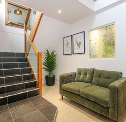 A staircase with black tiles next to a green sofa and potted plant with framed pictures on the wall at Swyn Llyr in Rhosneigr
