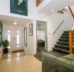 An entryway with a white front door a green plant a wall mirror and stairs next to a green sofa at Swyn Llyr in Rhosneigr