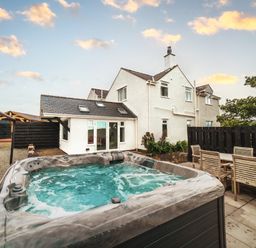 An outdoor area with a hot tub and seating near the house at Glanllyn Bach Llanfaelog