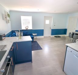 A kitchen and dining area with blue cabinets a corner sofa and a small dining table at Bluebell Cottage in St Brides-super-Ely near Cardiff