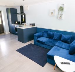 A kitchen with blue cabinets and a blue sofa with cushions and a small white table with a remote at Bluebell Cottage in St Brides-super-Ely near Cardiff