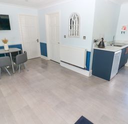 A kitchen area with a small dining table and chairs a wall-mounted TV and a kitchenette unit at Bluebell Cottage in St Brides-super-Ely near Cardiff