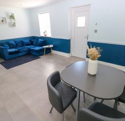 A dining area with four chairs and a table with a vase of flowers and a living area with a blue sofa and side tables at Bluebell Cottage in St Brides-super-Ely near Cardiff