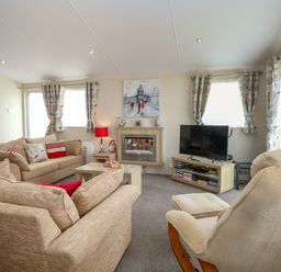 A living room with beige sofas a television fireplace and a rocking chair at 21 Norman Drive Lodge in Burgh Castle