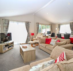 A living room with beige sofas a wooden coffee table a television and a dining table with red tablecloth at 21 Norman Drive Lodge in Burgh Castle