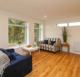 A living room with two sofas a coffee table a side table with a plant and windows showing greenery outside at The Farm Cottage in Athy County Kildare