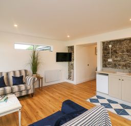 A living room with sofas a coffee table a small kitchen area and a mounted television at The Farm Cottage in Athy County Kildare