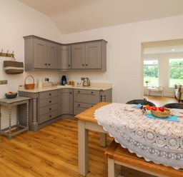 A kitchen with grey cabinets a small table with bowls a wooden dining table with a lace tablecloth and chairs at The Farm Cottage in Athy County Kildare