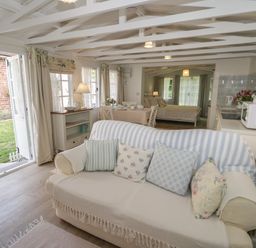 An open living space with a sofa and cushions a dining table and chairs a bed kitchen appliances and an open door leading to a garden at Ty Hafan in Mostyn