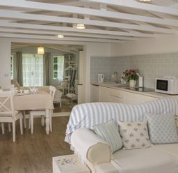 A living area with a sofa and cushions a dining table with chairs and a kitchen with appliances at Ty Hafan in Mostyn