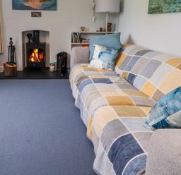 A living room with a sofa covered by a checkered blanket next to a fire stove and a television at Bryn Tirion in Morfa Nefyn
