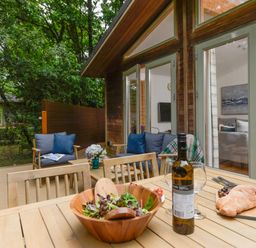An outdoor wooden patio with wooden chairs a table with salad bread wine glasses and sofas with cushions at 10 Stonerush Valley Lanreath near Looe