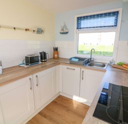 A kitchen with wooden countertops a black toaster a kettle a sink with a dish rack and a window with blue anchor blinds at The Sail Loft in Norton Park near Dartmouth