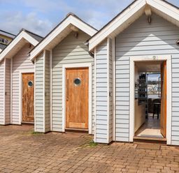 A row of small wooden beach huts with one open door showing an interior kitchen and sea view at Beach Hut 5 in Shaldon