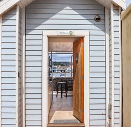 An open wooden door on a light blue beach hut showing a view of a chair and water beyond at Beach Hut 5 in Shaldon