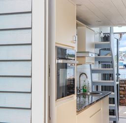A kitchen area with a sink oven dishwasher and stairs leading outside to a patio with a view of water and boats at Beach Hut 5 in Shaldon