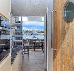 A small kitchen area with a countertop and sink next to a wooden door looking out to a dining table and chairs on a terrace overlooking water with boats at Beach Hut 5 in Shaldon