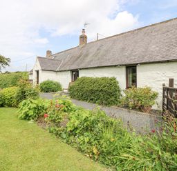 A garden with shrubs and flowers in front of a long white stone house with a slate roof at Loanview in Cornhill-On-Tweed