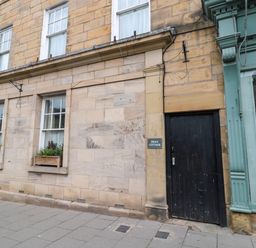 Exterior of a stone building with three windows and a black door with a sign reading Swan Cottage at White Swan Cottage in Alnwick
