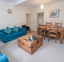 A living room with blue sofas, wooden coffee table, wooden dining table with chairs and a wall clock at White Swan Cottage in Alnwick