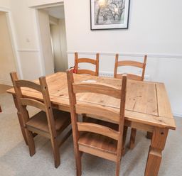 A dining room with a wooden table and four wooden chairs and a black armchair at White Swan Cottage in Alnwick
