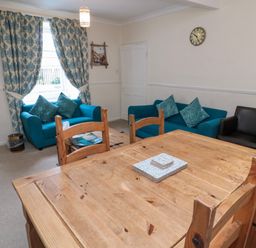 A living room with two blue sofas a black armchair a wooden dining table with chairs and patterned curtains at White Swan Cottage in Alnwick