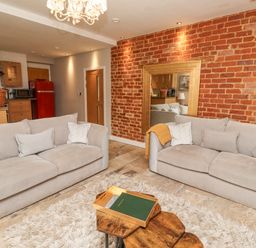 A living room with two beige sofas and a wooden coffee table on a rug with an exposed brick wall and a large mirror at The Fullerton in Belsay