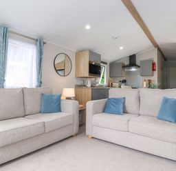 A living room with two beige sofas and blue cushions facing a kitchen area at Eltons Escape Pony Meadow 3 White Cross Bay near Windermere