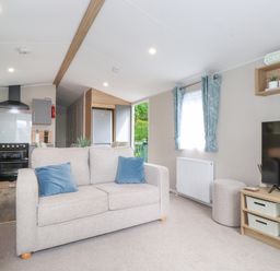 A living room with a beige sofa and blue cushions a television on a wooden stand and a kitchen area in the background at Elton's Escape in Pony Meadow 3 White Cross Bay near Windermere
