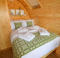 A bedroom with a bed covered in white bedding and green patterned pillows and blanket inside a wooden cabin at Moel Arthur in Bryniau Clwyd near Denbigh