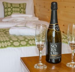 A bottle of prosecco and two empty glasses on a wooden table with a bed in the background at Moel Arthur in Bryniau Clwyd near Denbigh