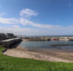 A harbor with boats docked near a sandy shore and buildings along the waterfront at Greenlee House in Seahouses